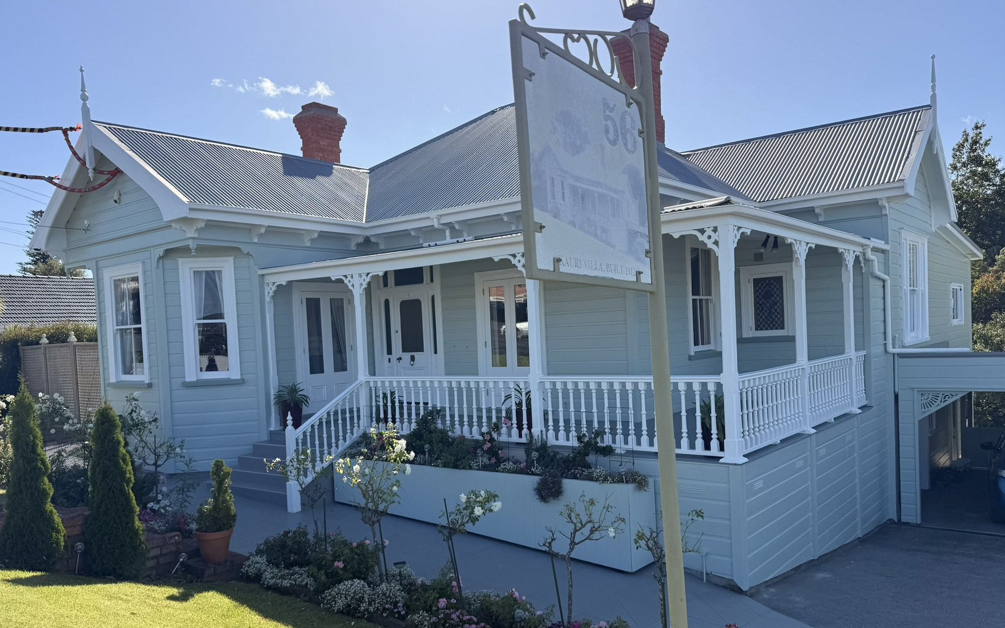 After: 1912 kauri villa in scaffold with faded sage weatherboards, then finished in soft duck-egg blue with crisp white trim and fretwork